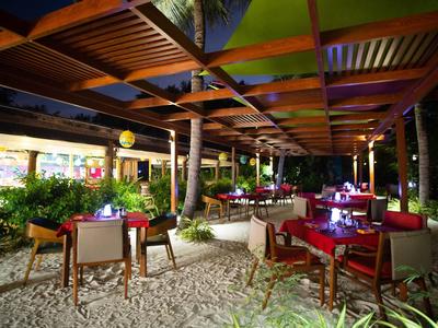 Outdoor hotel seating area with red tables, chairs, and hanging lights under a wooden roof.