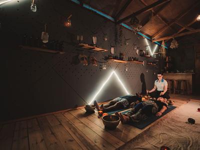 Cozy room with wooden floor, two people relaxing on mats, illuminated by warm light.