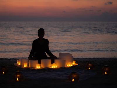 Person sitting on the beach surrounded by candles at sunset over the sea.