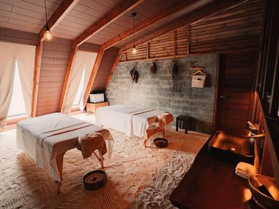 Warm spa room with two massage tables, wooden ceiling, and soft lighting.