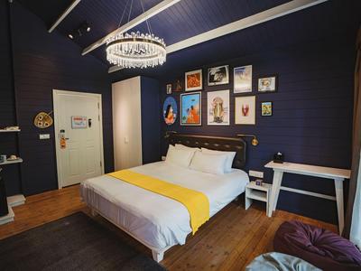 Modern hotel room with double bed, wooden floor, and decorative pictures on dark blue wall.