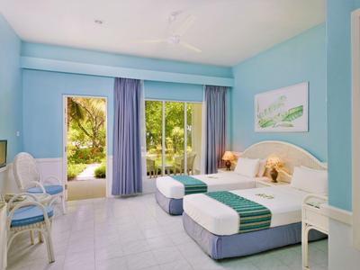 Světý hotelový pokoj s manželskou postelí, modrými závěsy a výhledem na zahradu.