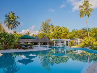 Großer Pool mit runden Inseln, umgeben von Palmen und gemütlichen Sitzbereichen unter blauem Himmel.
