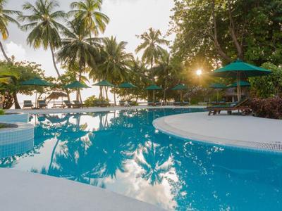 Pool with loungers and palm trees at sunset in a tropical resort.