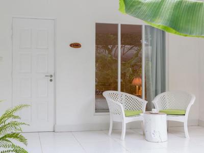 Světlá terasa s bílými židlemi, kulatým stolem a zelenými rostlinami u bílé stěny.