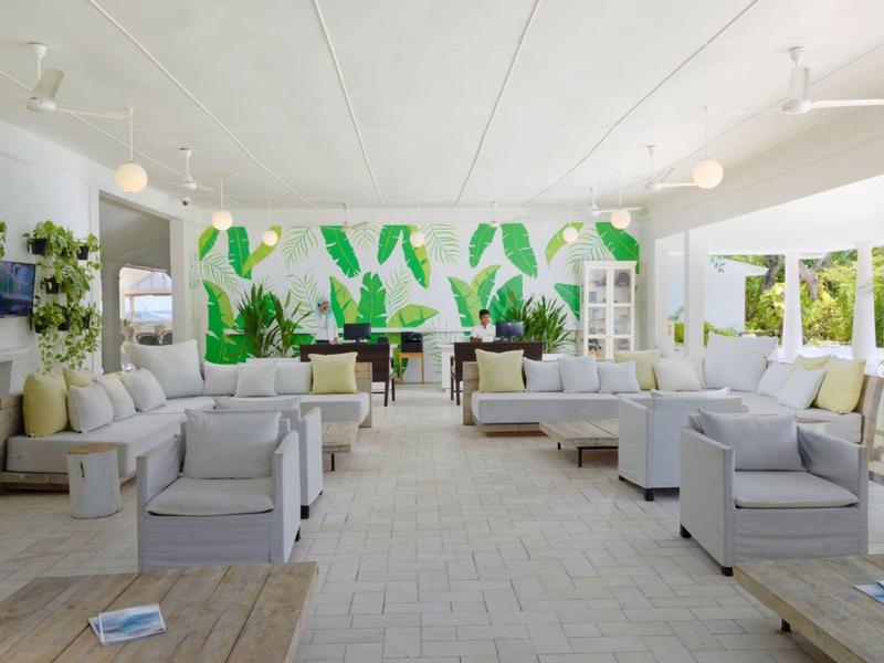 Světlý moderní venkovní salonek se šedými křesly a tropickou malbou na zdi.