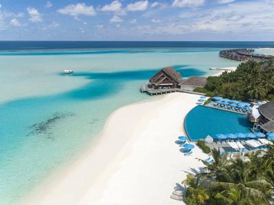 Strand mit weißem Sand, türkisfarbenem Wasser, Palmen und Schwimmbad bei klarem Himmel.