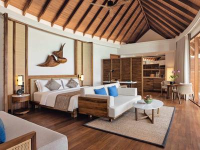 Velký hotelový pokoj s dřevěnou podlahou, dvojlůžkem, pohovkou a balkonem se skleněnou stěnou.