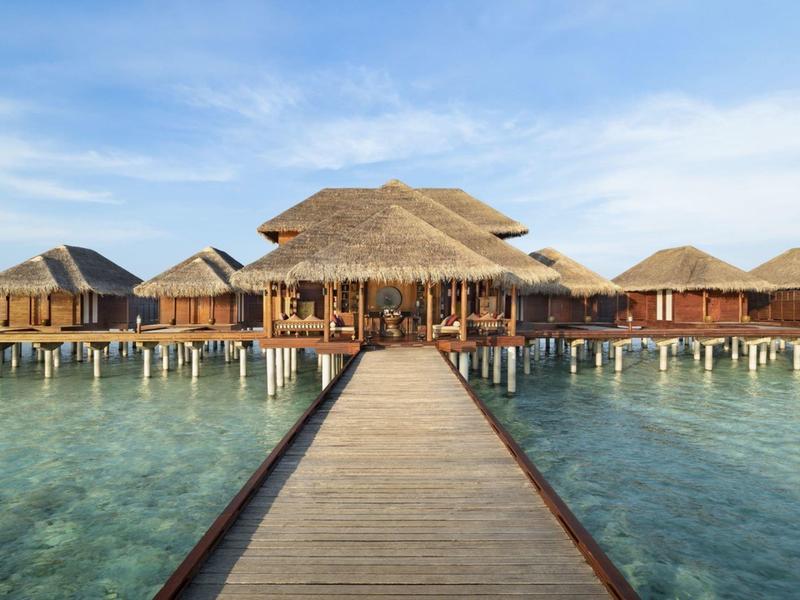 Dřevěný mole vede k bungalovům postaveným na vodě v průzračném mělkém moři.