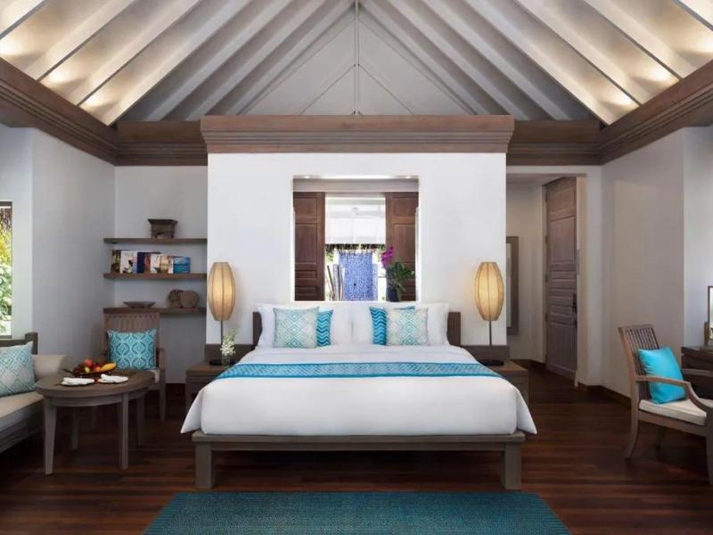 Světý hotelový pokoj s manželskou postelí, dřevěným nábytkem a modrými doplňky.