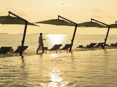 Persona camina junto a piscina con tumbonas y sombrillas al atardecer.
