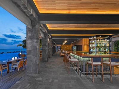 Moderner Hotel-Außenbereich mit Bar, Sitzgelegenheiten und Blick auf das Meer bei Sonnenuntergang.