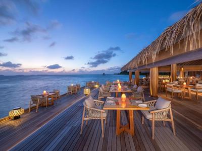 Freiluft-Restaurant am Wasser mit Holzboden und Strohbedachung bei Sonnenuntergang.