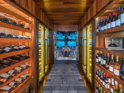 Pasillo con paredes de madera iluminadas y estantes de vino, vista a terraza exterior con mesa y sillas.