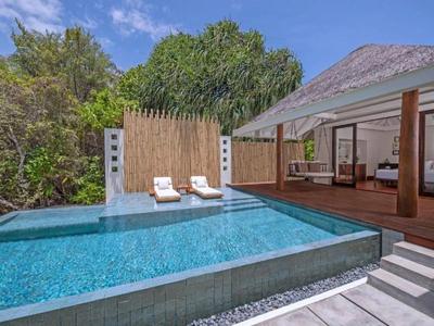 Área moderna de piscina con tumbonas y un salón abierto en un hotel tropical.