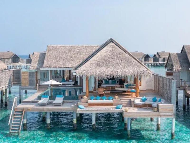 Bungalows de lujo sobre el agua con pasarelas de madera y agua turquesa clara bajo un cielo azul.
