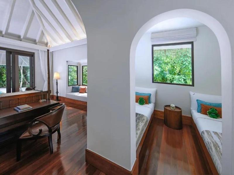 Habitación de hotel luminosa con suelo de madera, escritorio y dos camas individuales en una habitación separada.