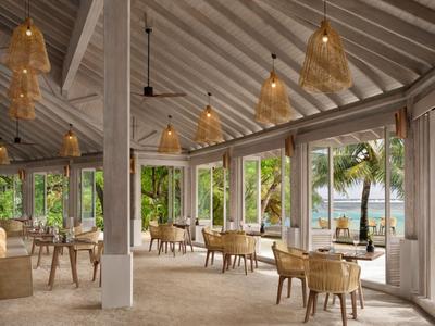 Espace de restaurant ouvert avec chaises et tables, vue sur les palmiers et la mer.