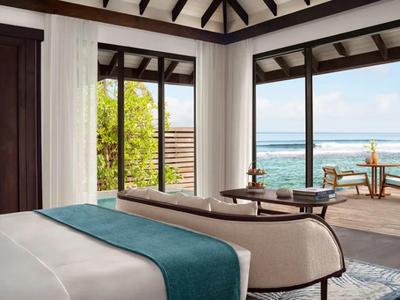 Jasny pokój hotelowy z widokiem na morze i balkonem z miejscami do siedzenia.