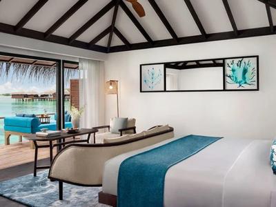 Jasny pokój hotelowy z dużym łóżkiem, niebieskimi akcentami i widokiem na basen oraz plażę.