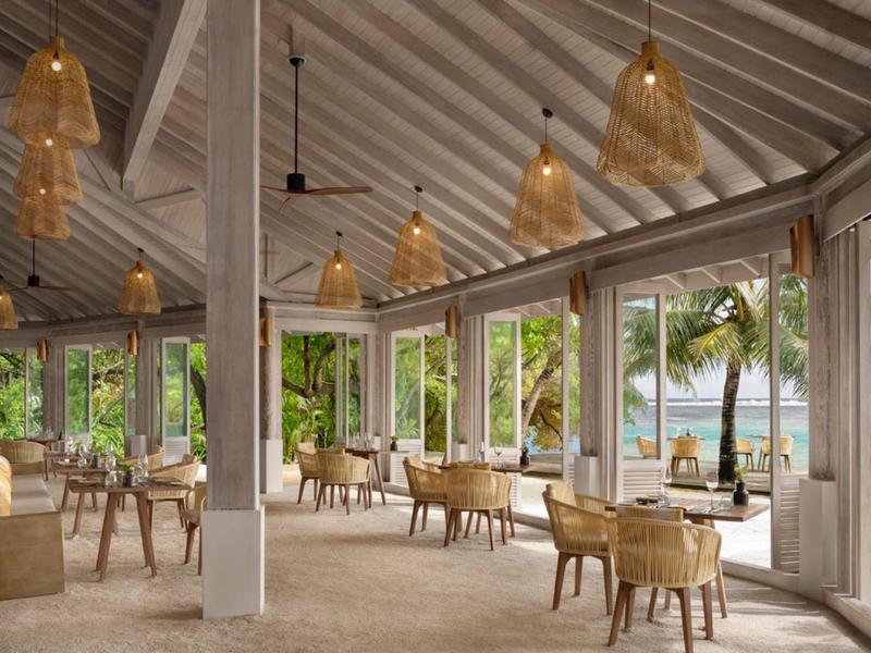 Otwarta część wypoczynkowa hotelu z meblami z rattanu i widokiem na palmy i morze.