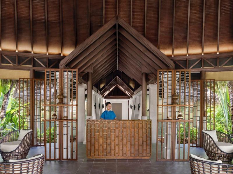 Otwarta recepcja hotelowa z tropikalną atmosferą i drewnianym kontuarem, otoczona miejscami do siedzenia.