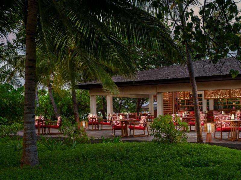 Wieczorny taras hotelu z nakrytymi stołami i bujną zieloną roślinnością.