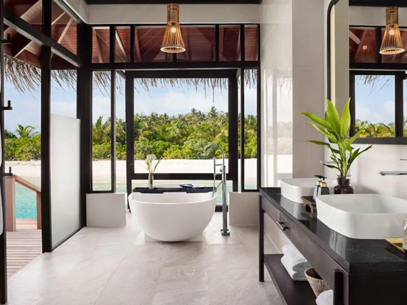 Nowoczesna łazienka hotelowa z wolnostojącą wanną i widokiem na ogród i basen.