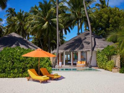Strandresort met palmbomen, rieten hutten, ligstoelen en een oranje parasol.