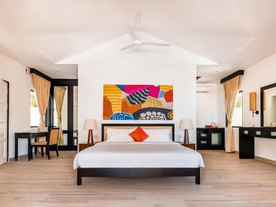 Lichte hotelkamer met groot bed, kleurrijke kunst, houten vloer en elegante meubels.