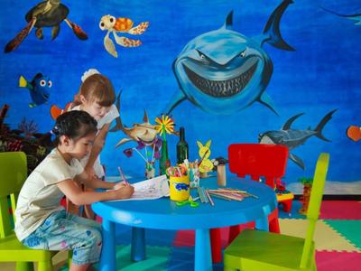 Kinderen kleuren aan een blauwe tafel met haaienmuurdecoraties in een speelkamer.