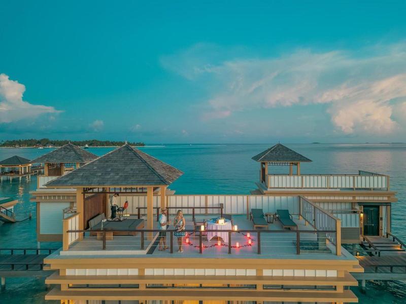 Luxe bungalows op het water met zitgedeeltes en uitzicht op de oceaan onder een blauwe lucht.