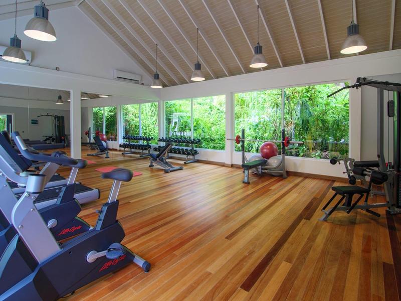 Geräumiges Fitnessstudio mit Holzboden, großen Fenstern und verschiedenen Trainingsgeräten.