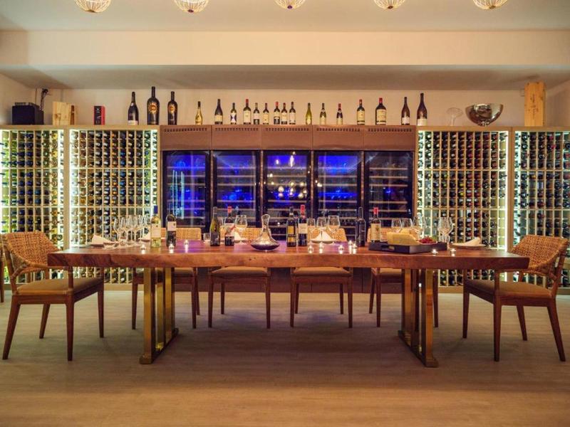 Moderner Verkostungsraum mit Holztisch, vier Stühlen und beleuchteten Weinregalen im Hintergrund.