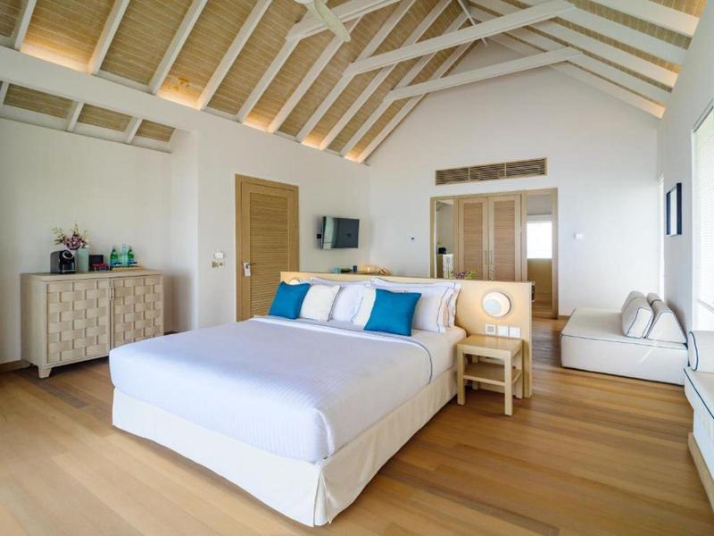 Helles Schlafzimmer mit Holzboden, großem Bett, weißer Kommode und eingebautem Fensterbereich.