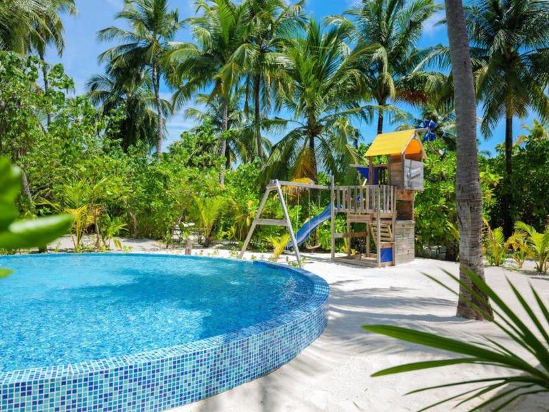 Rundpool mit Mosaikfliesen, umgeben von Palmen und einem Spielplatz mit Rutsche im tropischen Garten.