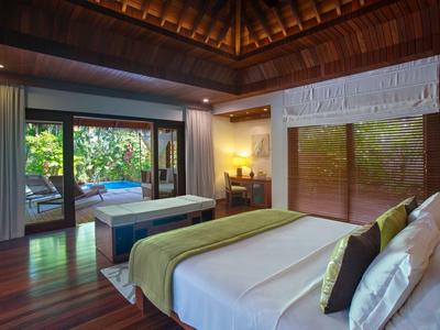 Cozy hotel room with wooden decor, large bed, and a view of a private pool and garden.