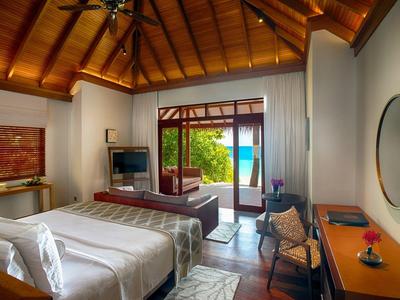 Spacious hotel room with wooden ceiling, bed, desk, TV, and sliding doors opening to a garden view.