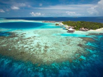 Aerial view of a tropical island resort surrounded by clear turquoise waters and coral reefs.