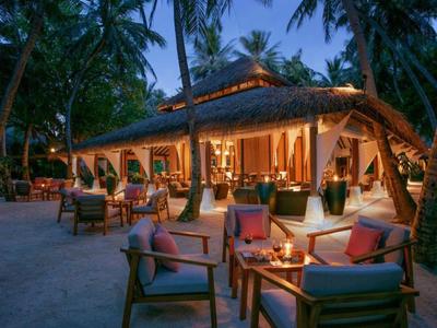 Cozy outdoor hotel seating with candles and cushions under palm trees at dusk.