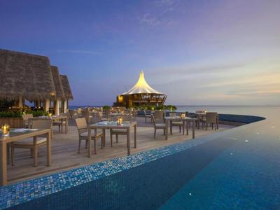 Outdoor pool with seating area and lit building at twilight by the sea.