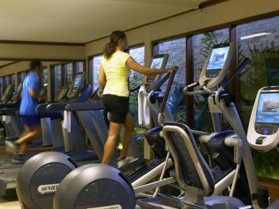 Due persone si allenano su macchine cardio in una palestra moderna con grandi finestre.