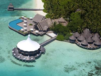 Tropisches Resort mit Wasserbungalows, Pool und grüner Vegetation auf klarem türkisfarbenem Wasser.