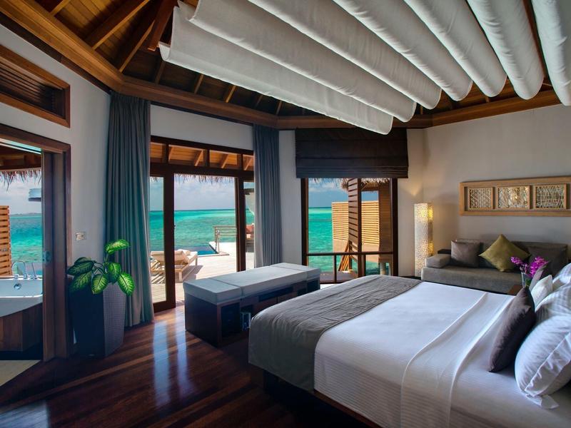 Spacious bedroom with large windows overlooking the ocean and patio area, wooden floors and ceiling.