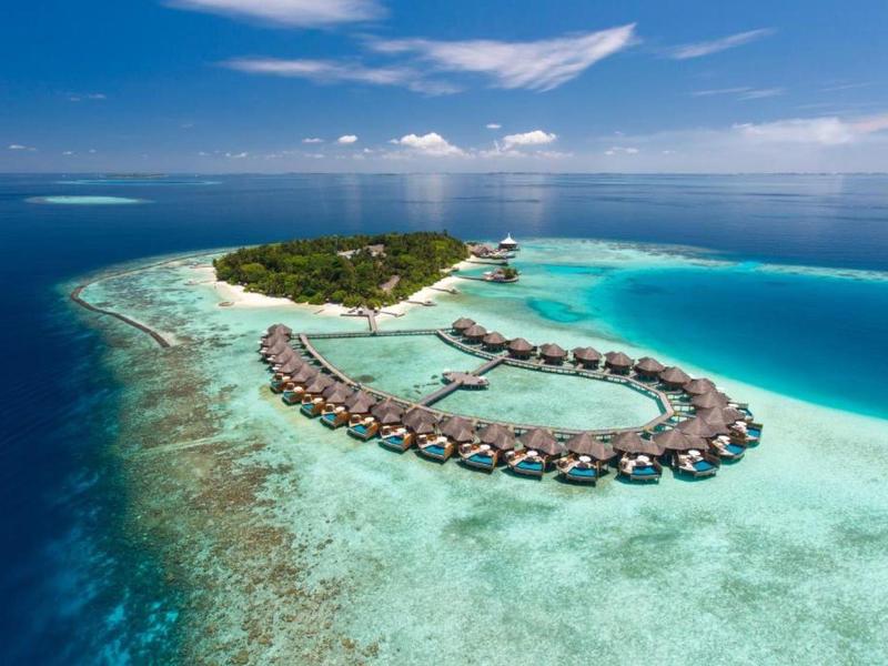 Aerial view of an island resort with overwater bungalows surrounded by clear blue ocean.