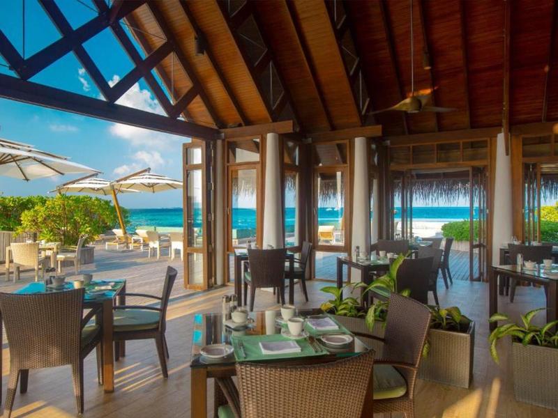 Covered and open patio dining area with tables, chairs, and ocean view under blue sky.