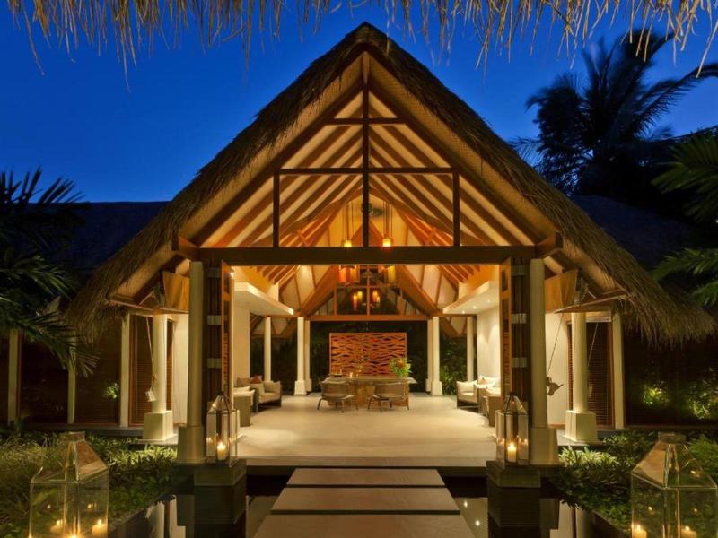 Night view of a warmly lit tropical bungalow with wooden beams and thatched roof.