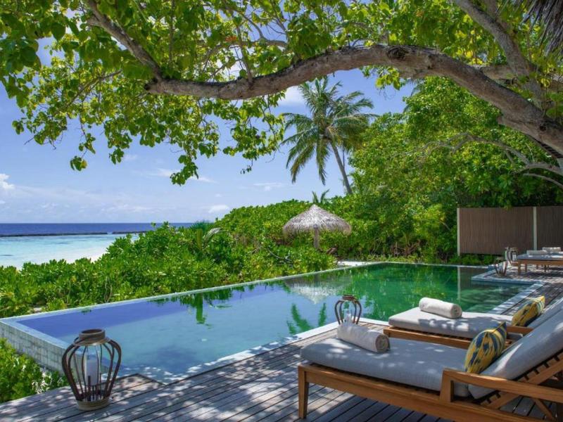 Scenic poolside lounge overlooking tropical greenery and ocean under a clear blue sky.