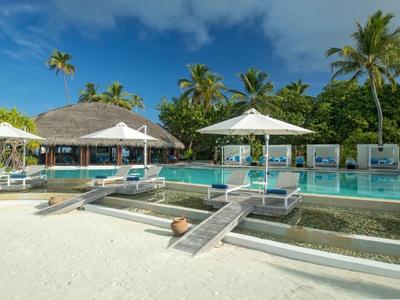 Přímořské letovisko s bazénem, lehátky a palmami pod modrou oblohou.