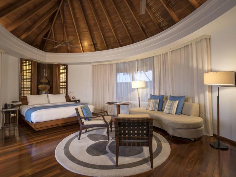 Camera d'hotel rotonda con pavimento in legno, grande letto e comoda zona soggiorno.